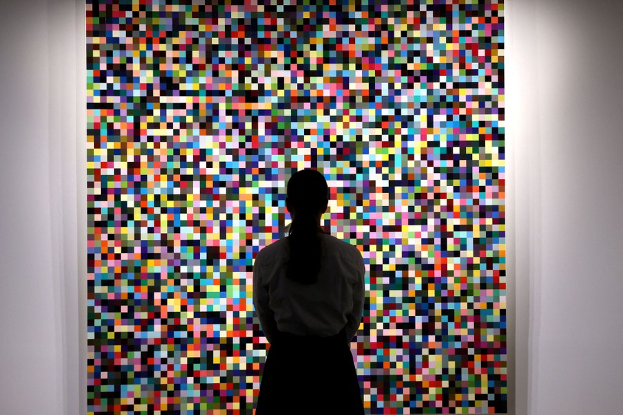 A person stands before a work of art made up of hundreds of small colored squares.