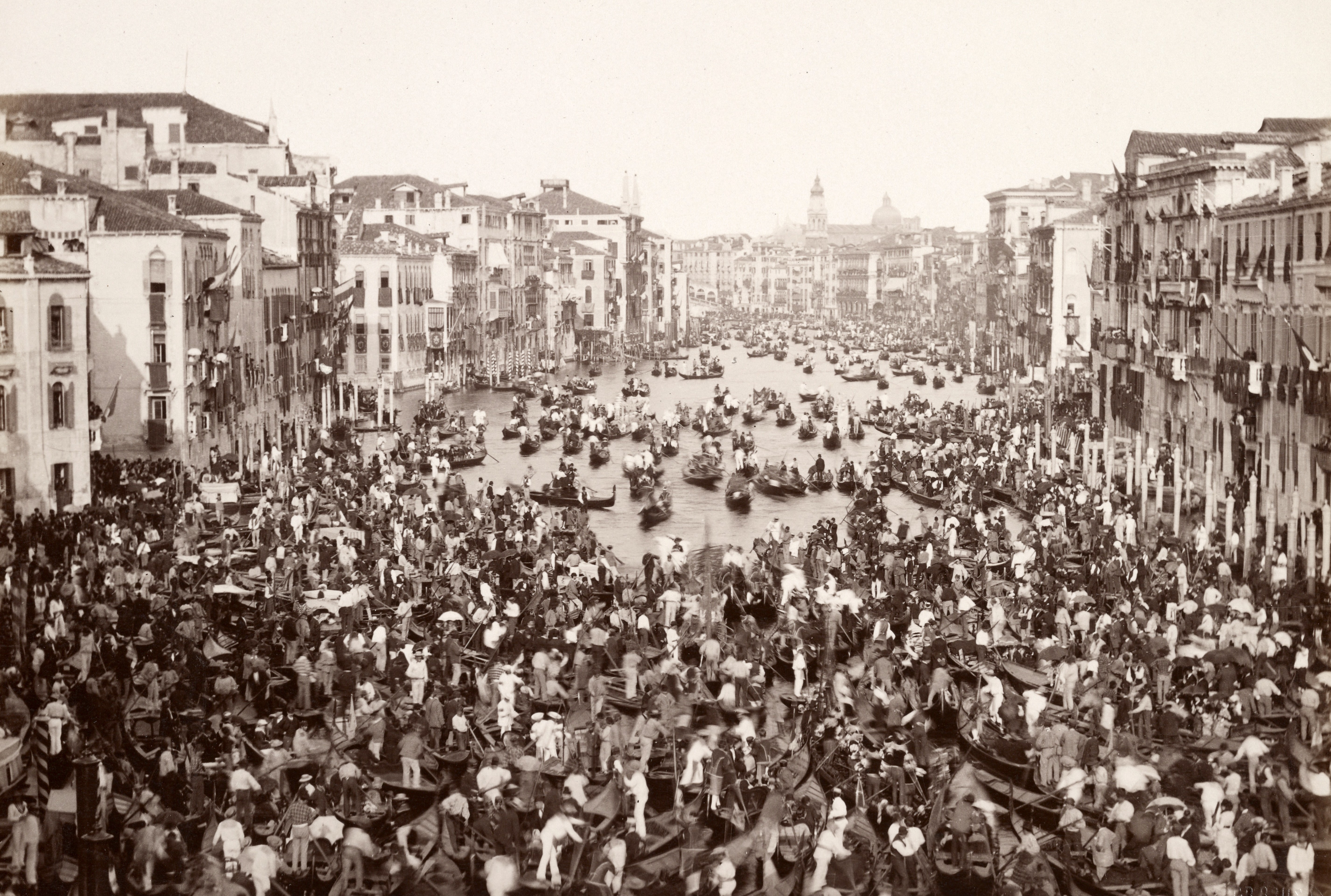Hundreds of small boats and rowers cluster together in a broad canal in Venice.