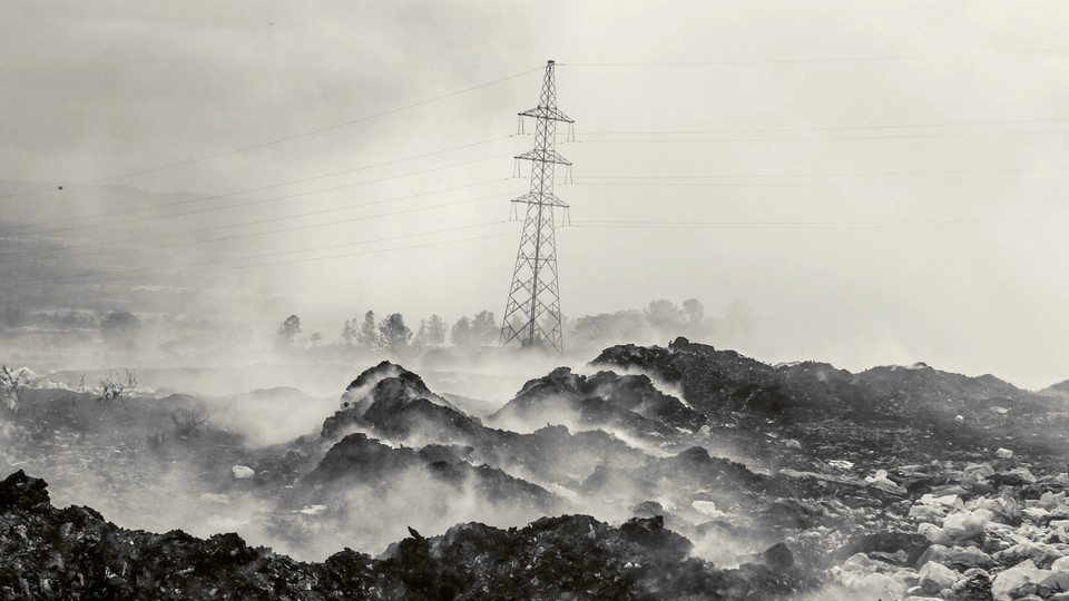 A high-voltage electricity pylon behind a plume of smoke from burning garbage, mostly plastic and textiles, at the Gioto dumpsite