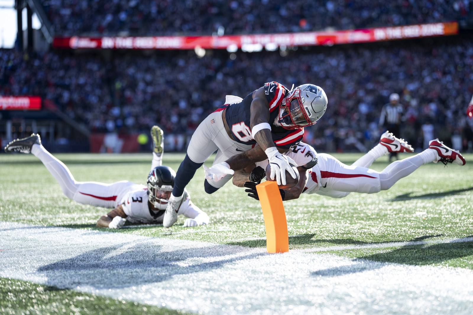 A football player dives for the end zone, holding the ball out and hitting a small soft pylon on the boundary line.