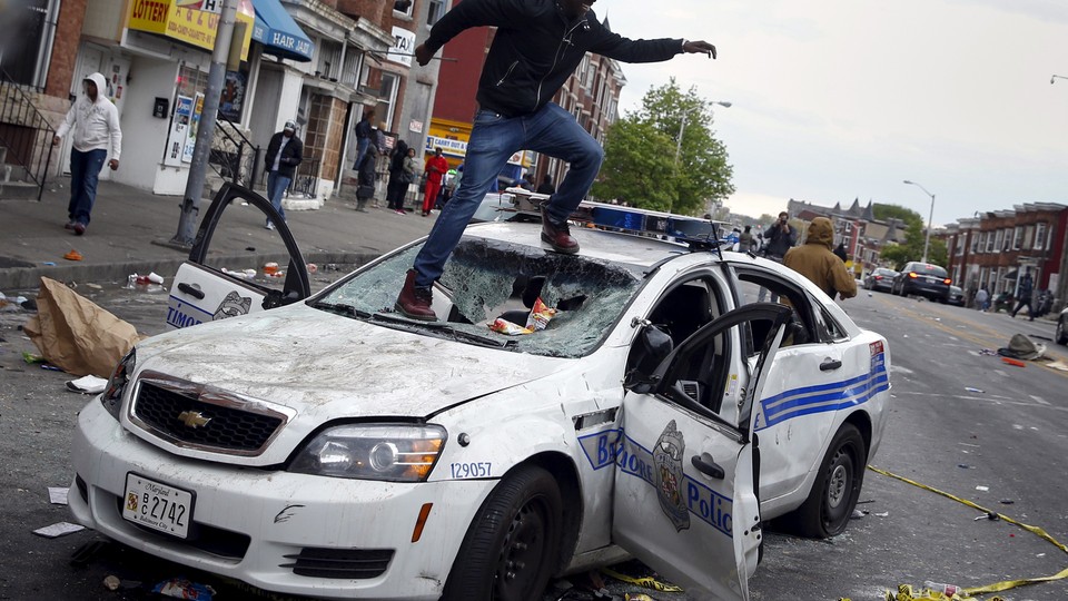 A man jumps on a destroyed Baltimore Police car during protests after the death of Freddie Gray.