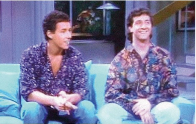video still of young Adam Sandler and Judd Apatow smiling and wearing printed floral button-downs and jeans, sitting on blue couch 