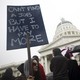 Woman stands with a sign that reads "Can't find a job but I have to pay more" in California