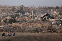 Photograph of destroyed buildings in Gaza with people sitting on the roadside staring at the wreckage