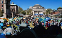 Pro-Palestinian protesters sit and stand, some in front of tents, in a large grassy area at Columbia University.