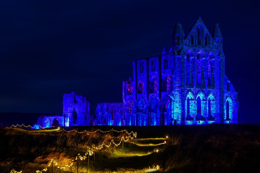 The ruins of an old abbey are lit up in blue, seen at night.