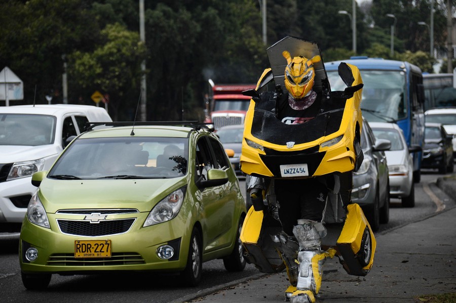 A person walks on a sidewalk wearing a costume that looks like several car parts.