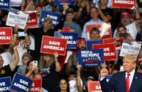 Donald Trump raises a fist, a crowd of supporters holding "save America!" signs stand behind him.