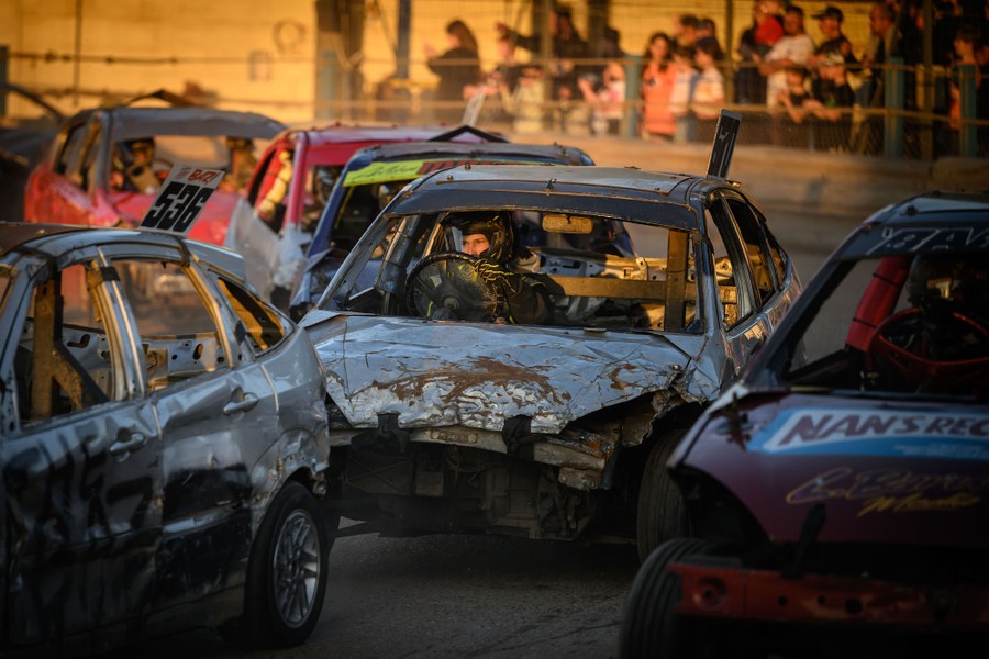 Drivers race beat-up cars in a stadium.