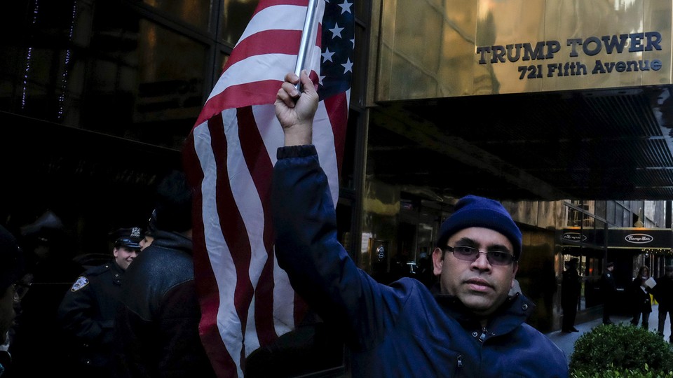 A Muslim man stands waving an American flag in front of the Trump Tower sign.