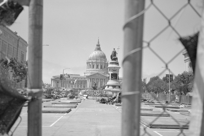 mattresses on the ground in front of city hall seen through a chain linked fence