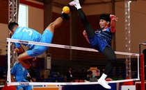 Two athletes leap high into the air to kick a small ball over a net.