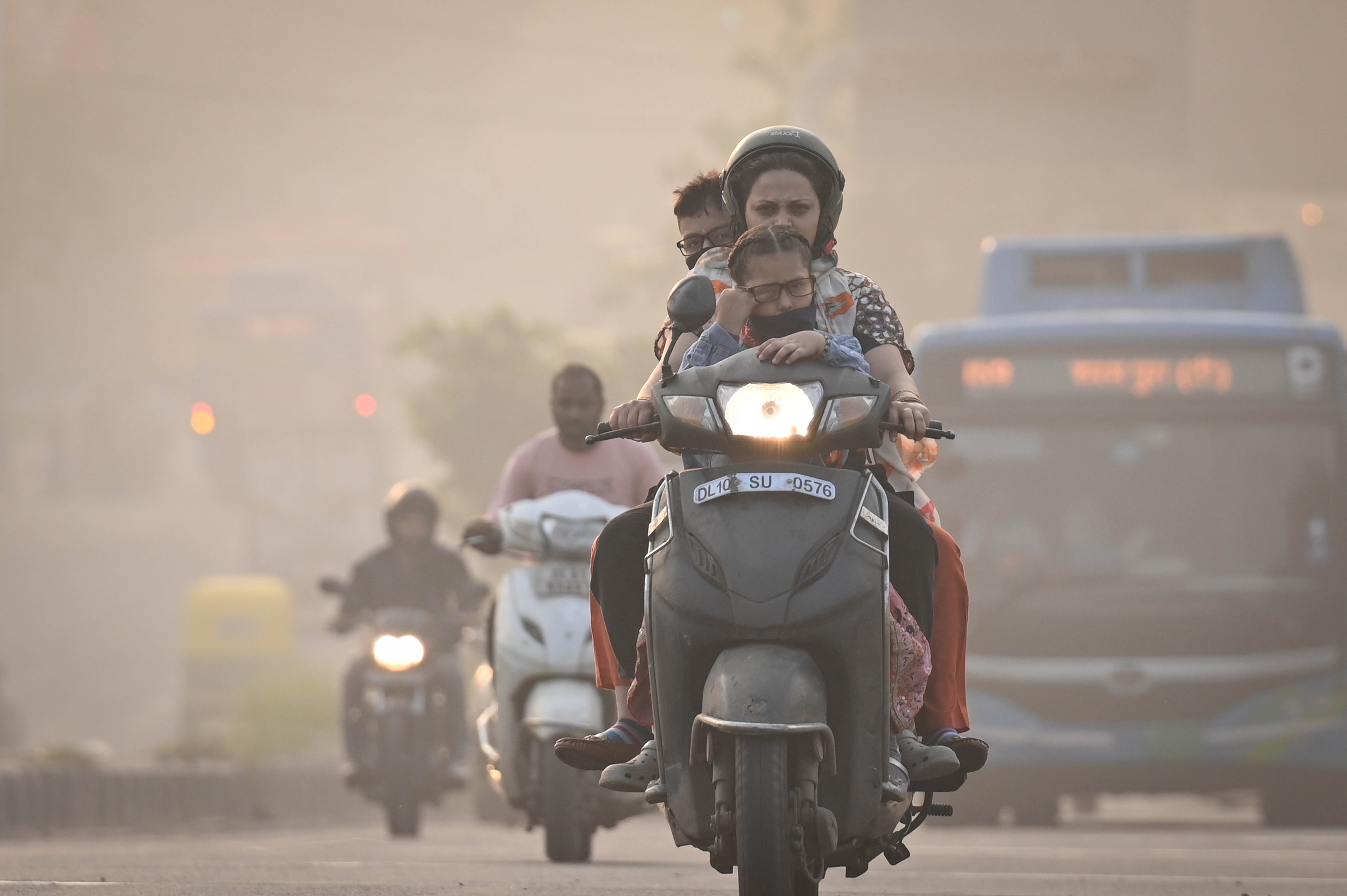Several people drive scooters down a road through smoggy air.
