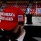 An image of a man wearing a MAGA hat in front of a stage with signs that read "In Memory of Charlie Kirk"