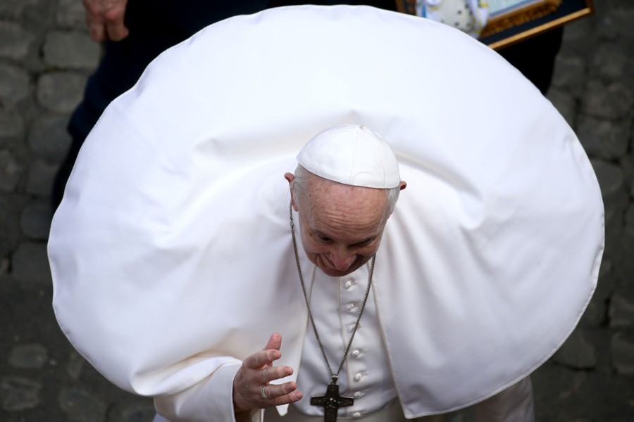The wind gusts as Pope Francis greets pilgrims in a courtyard.