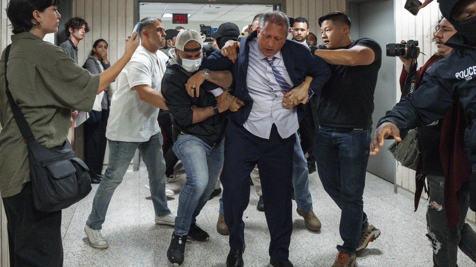 An image of Brad Lander being pulled down the hallway of a federal courthouse