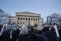 Students hold signs reading "resist" outside a stately university building with grand columns.