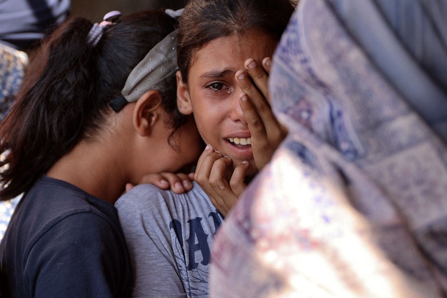 Two children lean close to each other, and one cries, as they shelter during an airstrike.