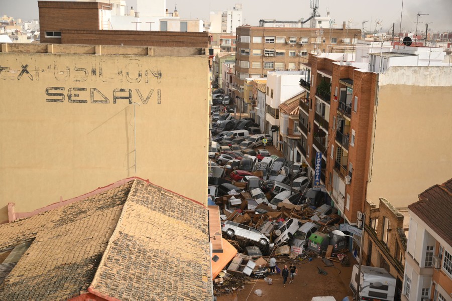 A city street is filled with a jumble of cars and flood debris.