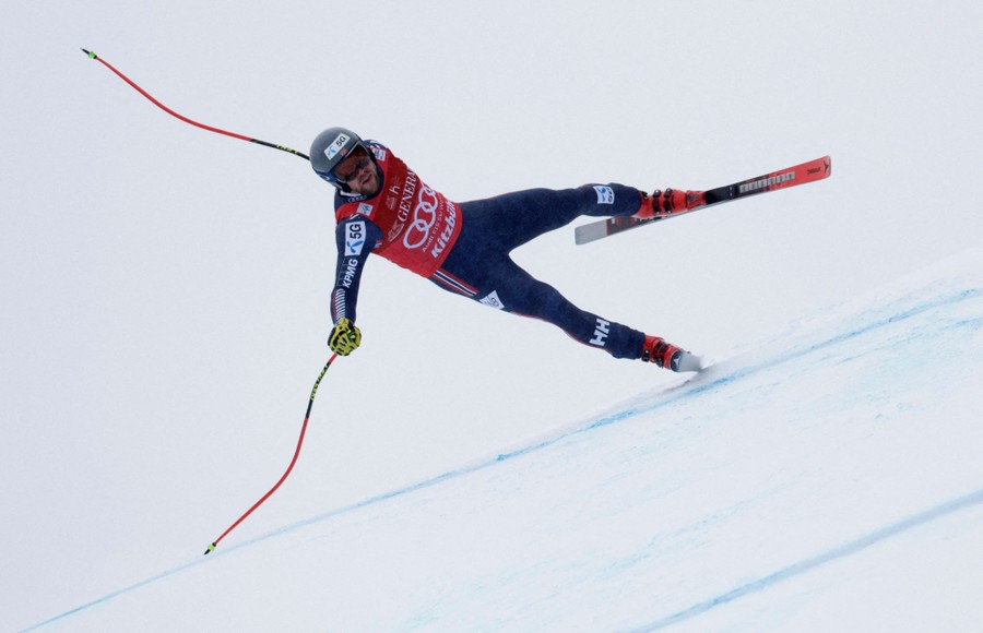 A downhill skier leans heavily, balancing on one leg, during a run.