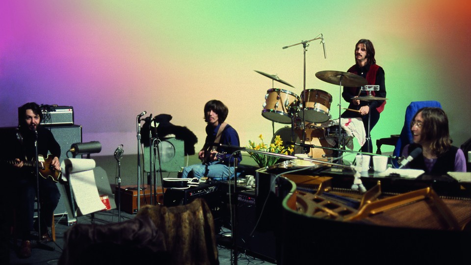 The Beatles sit at a variety of instruments, playing.