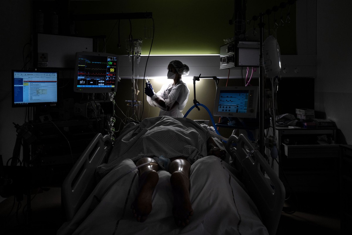 A nurse stands beside a bed with a patient lying in it.