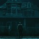 man in a suit stands in front of a spooky house at night