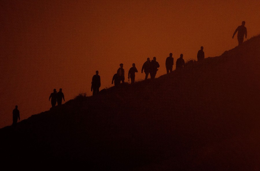About a dozen migrants climb a cliffside.