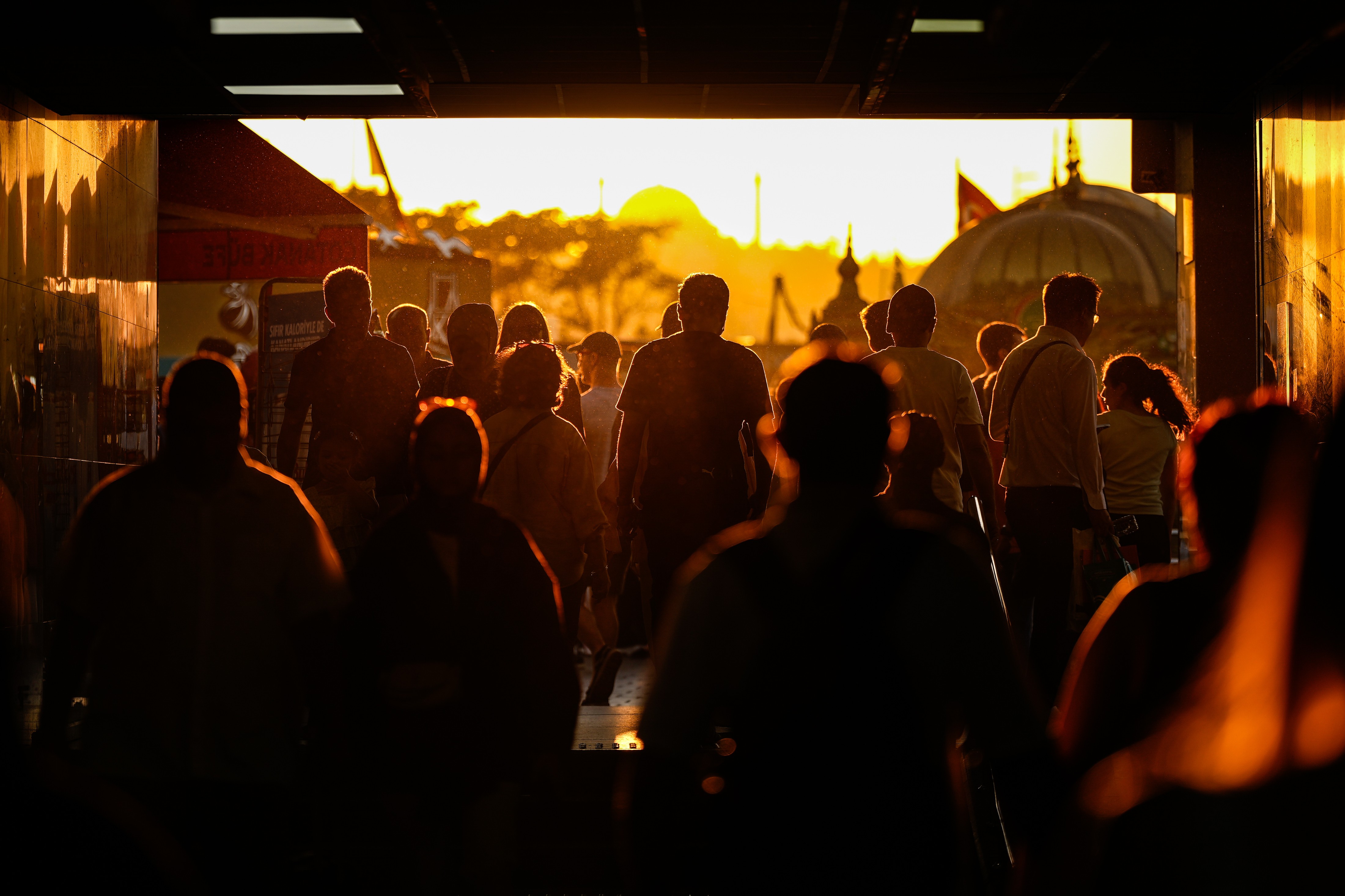 People walk through an underpass, lit by a low sun.
