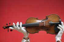 A person wearing white gloves holds up a violin