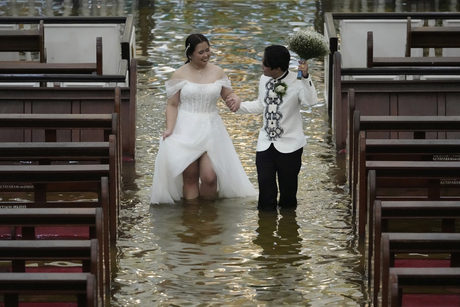 A newlywed couple walks together down a flooded church aisle.