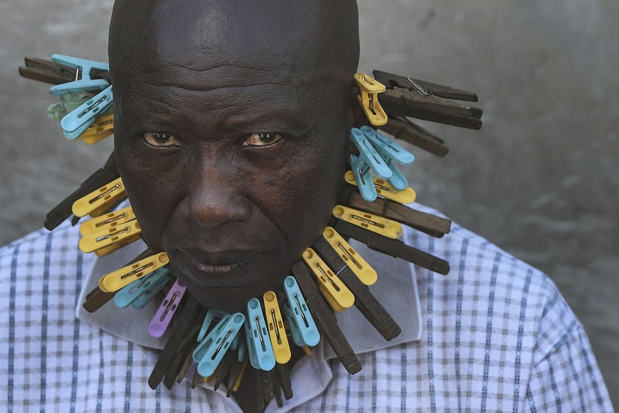 A man is photographed with more than 30 clothespins pinching his cheeks, chin, and ears.