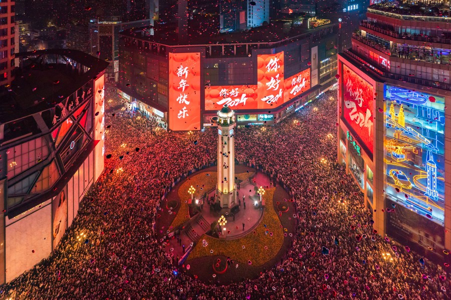A crowd of people fills a city square, captured from above.