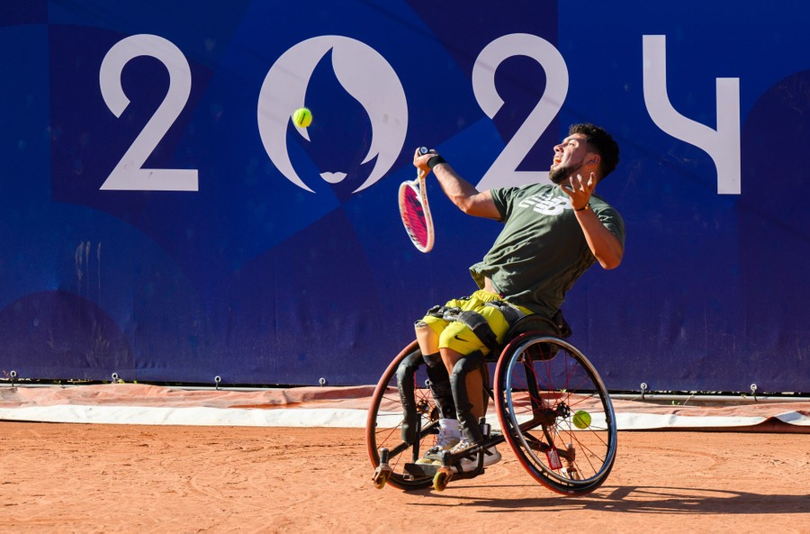 An athlete in a wheelchair swings a racket at a tennis ball on a court.