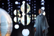 A person stands inside a dark room, looking at suspended globes, lit up in an exhibition.