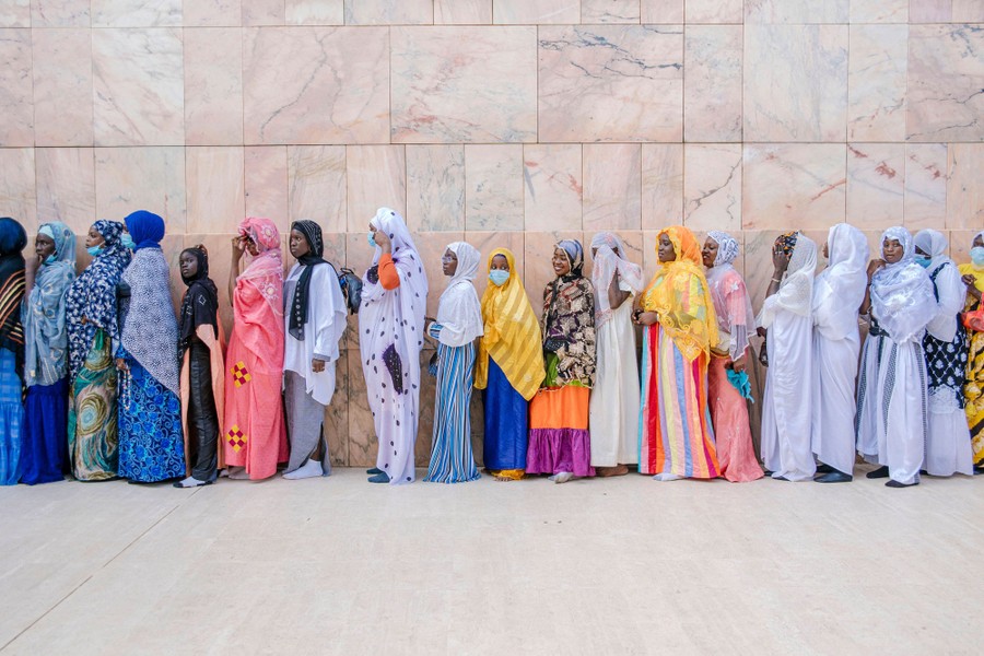Dozens of women line up against a marble wall.