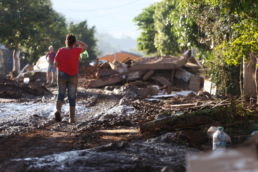 Several people walk on muddy roads past flood debris.