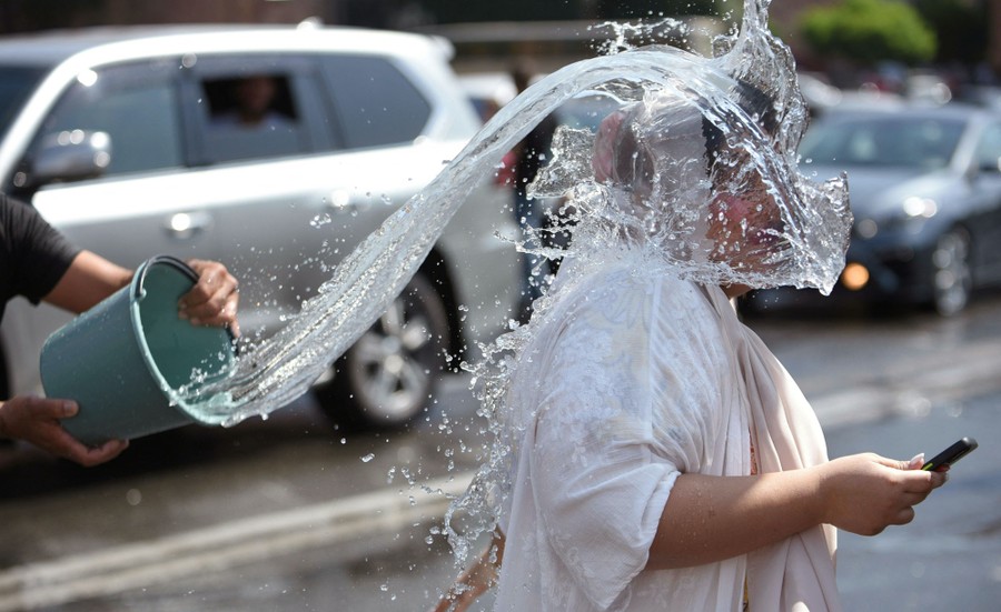 A person throws water from a bucket onto another person's head and back as they walk away.