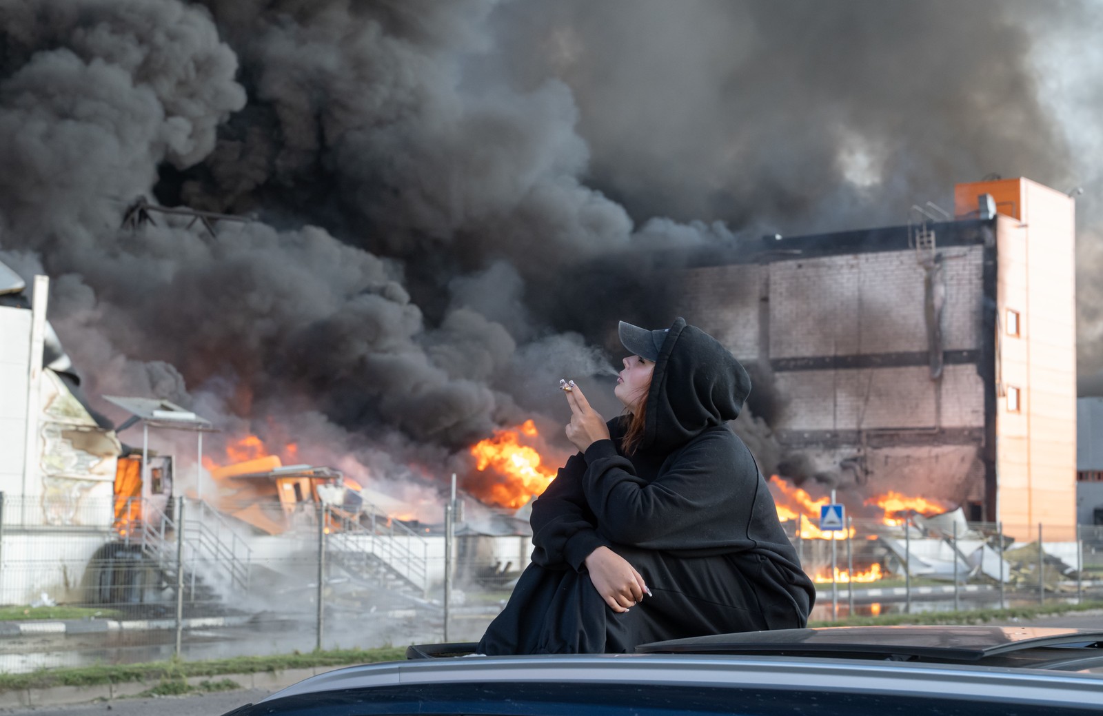 A woman smokes while watching a burning warehouse.