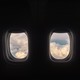 A row of airplane windows show a cloudy sky