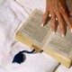 An older person's hand holds a book open on a towel.