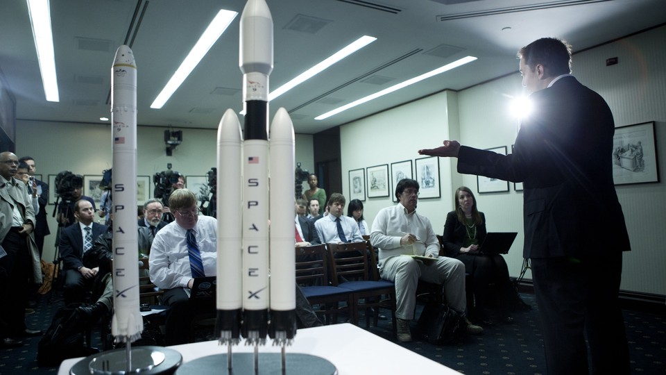 A person gestures to two models of rockets labeled "SpaceX."