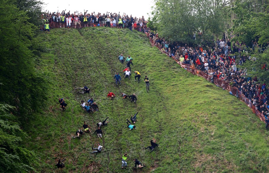 A wide view of runners racing down a very steep grassy hill as a surrounding crowd cheers