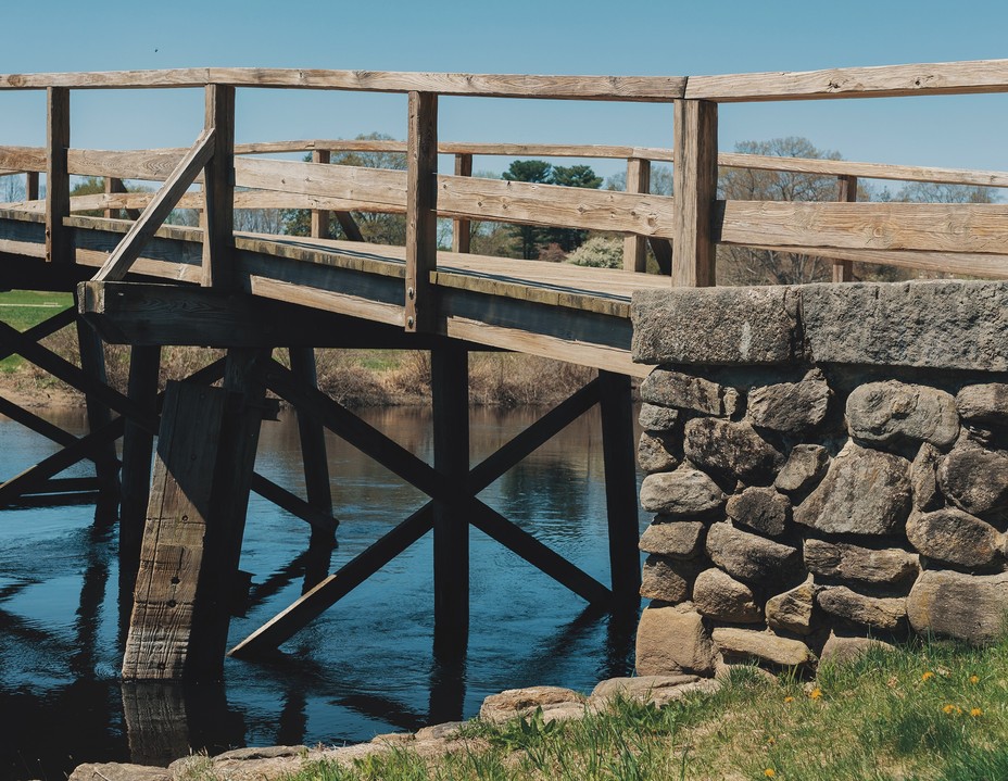 photo from bank of low wooden bridge with railing and stone landing