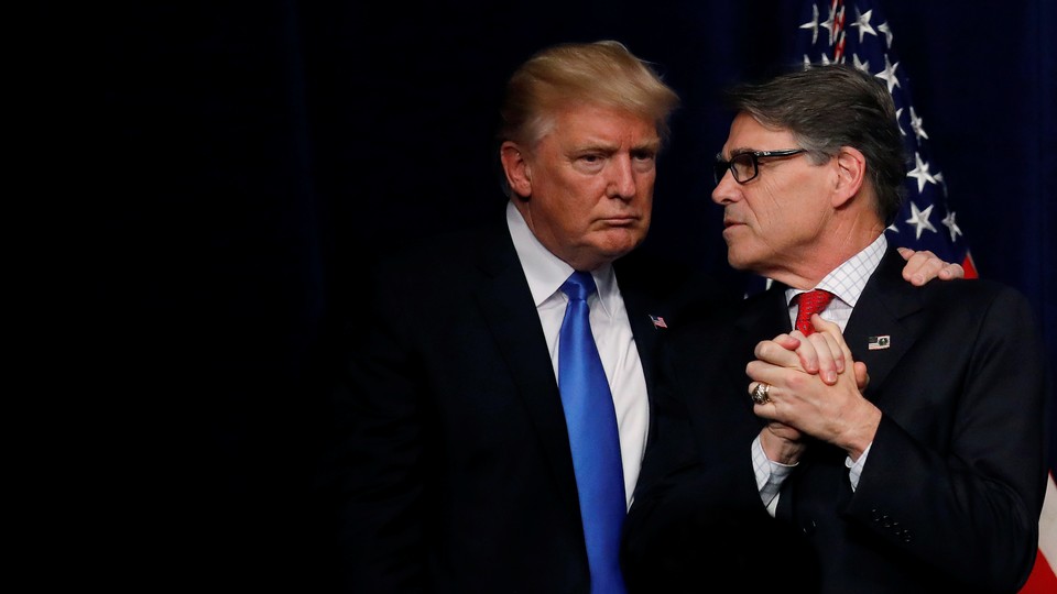 President Donald Trump huddles with Secretary of Energy Rick Perry in front of a curtain and an American flag.