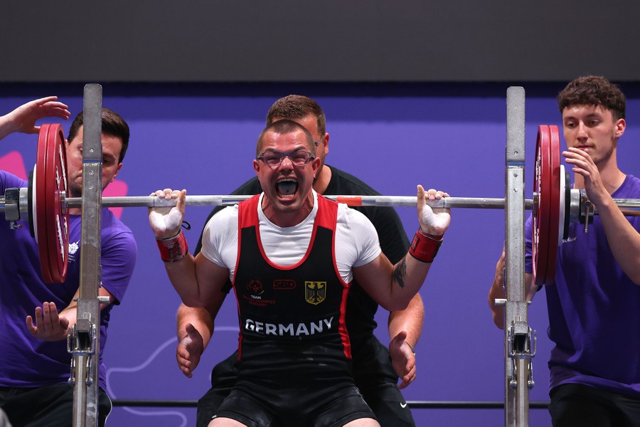 A weightlifter strains and makes a face while lifting weights.