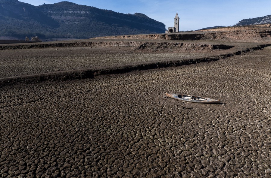 An abandoned kayak lies on cracked ground in a dried-out reservoir.