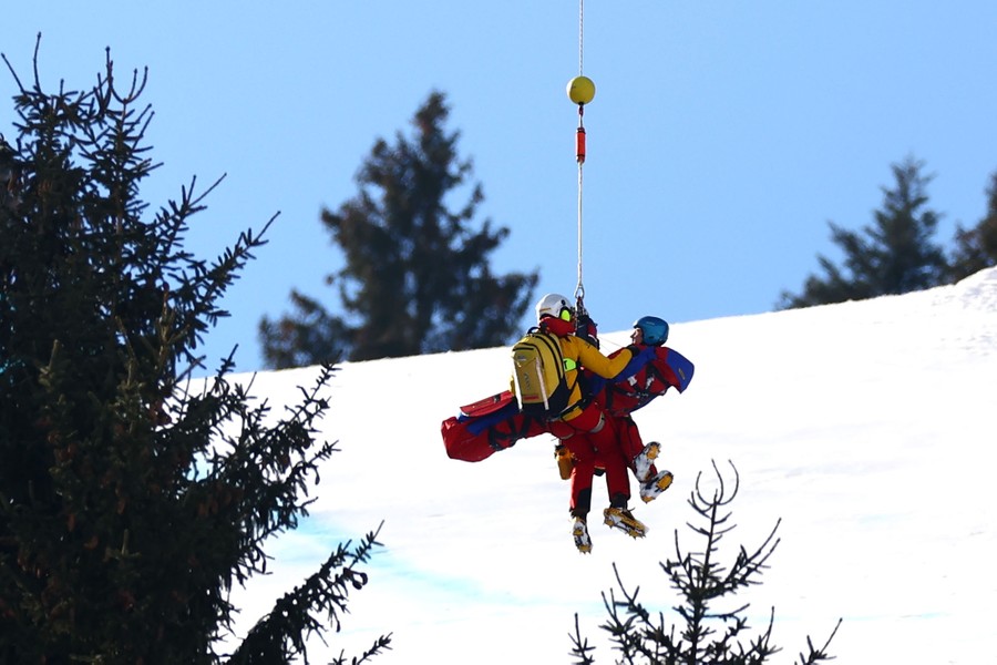 Two people are lifted from a snowy mountain slope by a cable.