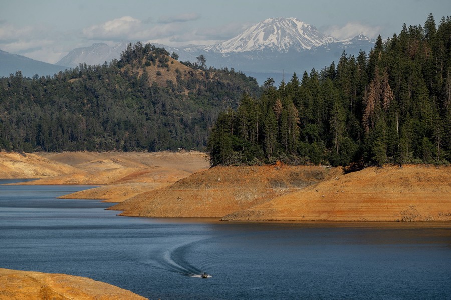 A small boat moves along the surface of a reservoir, which stands at about half its capacity.