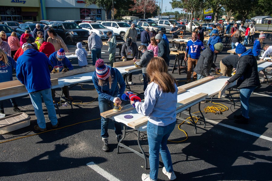 Dozens of people work at temporary tables in a parking lot, sanding pieces of lumber for beds.